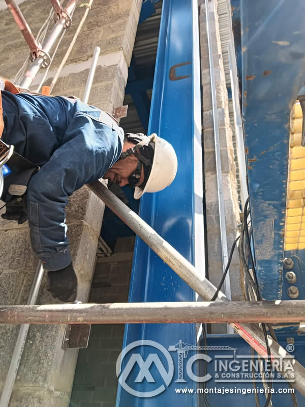 Inspección de viga metálica en altura con arnés de seguridad en planta industrial en Bogotá, Colombia. Montajes, Ingeniería y Construcción MIC SAS.
