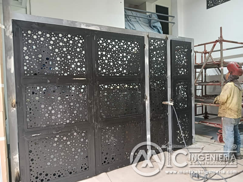 Soldadura en instalación de portones metálicos perforados decorativos en local comercial en Bogotá, Colombia. Montajes, Ingeniería y Construcción MIC SAS.