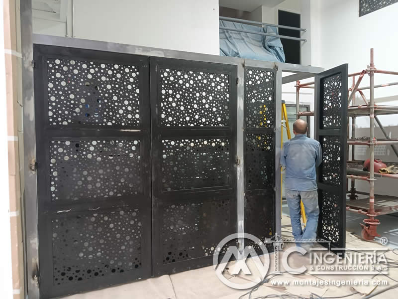 Verificación y ajuste de portones metálicos perforados durante su instalación en local comercial en Bogotá, Colombia. Montajes, Ingeniería y Construcción MIC SAS.