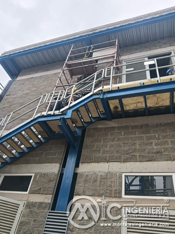 Escalera metálica azul de dos tramos con rejilla FRP en fachada de planta industrial en Bogotá, Colombia. Montajes, Ingeniería y Construcción MIC SAS.