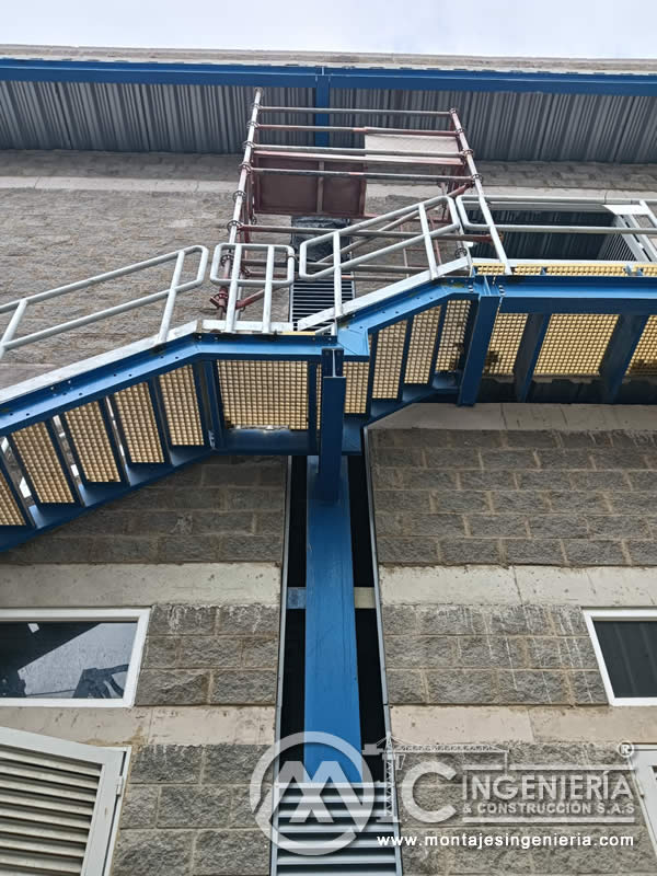 Escalera metálica azul de tres tramos con rejilla FRP y louver en fachada industrial en Bogotá, Colombia. Montajes, Ingeniería y Construcción MIC SAS.
