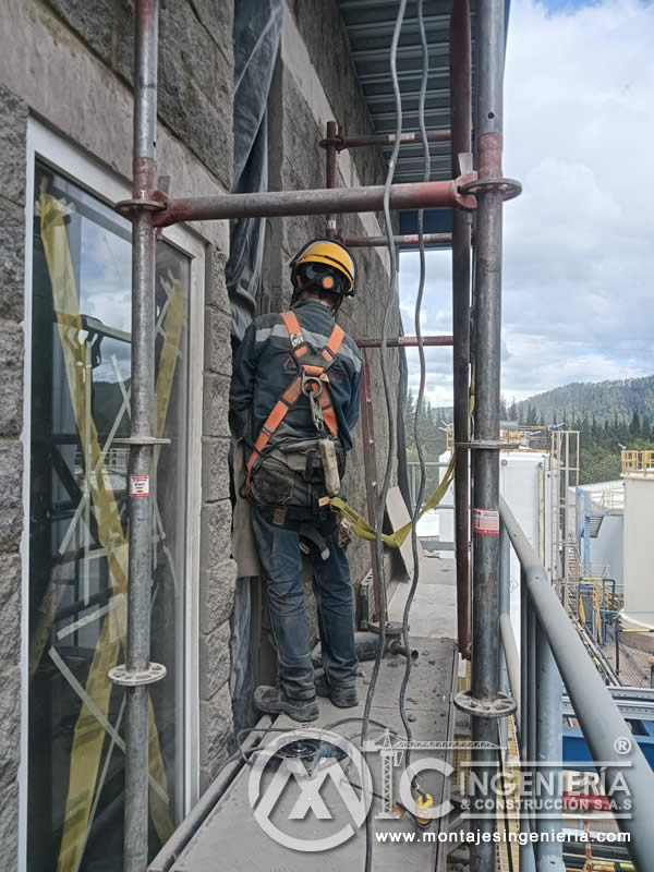 Técnico con arnés instalando elementos en fachada de planta eléctrica en Bogotá, Colombia. Montajes, Ingeniería y Construcción MIC SAS.