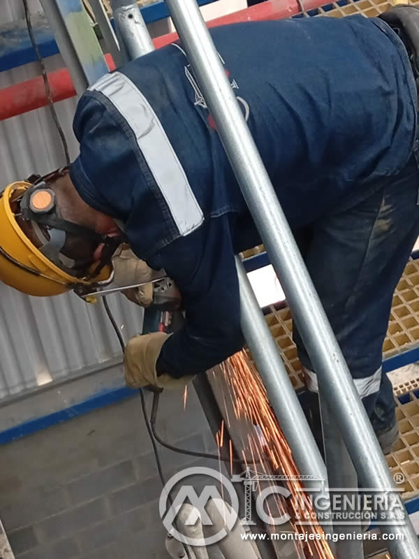 Esmerilado y acabado de tubería galvanizada sobre plataforma de rejilla en planta industrial en Bogotá, Colombia. Montajes, Ingeniería y Construcción MIC SAS.