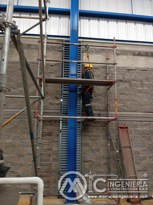 Montaje de elevador industrial con arnés de seguridad y línea de vida sobre andamios certificados en Bogotá, Colombia. Montajes, Ingeniería y Construcción MIC SAS.
