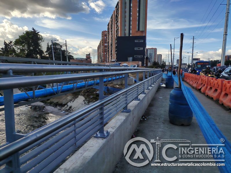 Proteja peatones, canal y tránsito mediante una baranda gris instalada sobre el muro de concreto urbano en Bogotá, Colombia. Montajes, Ingeniería y Construcción. MIC SAS.