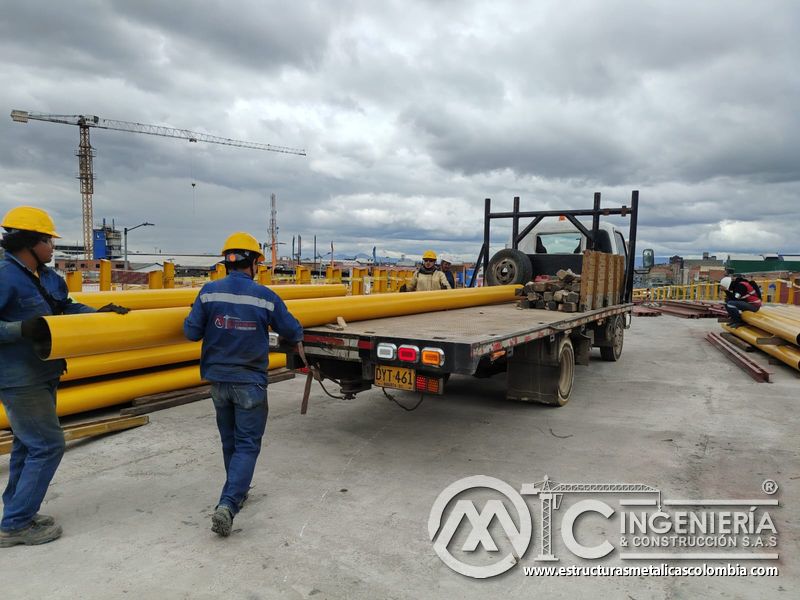 Observe a dos trabajadores conducir un tubo largo desde el camión hasta el sector de montaje del puente en Bogotá, Colombia. Montajes, Ingeniería y Construcción. MIC SAS.