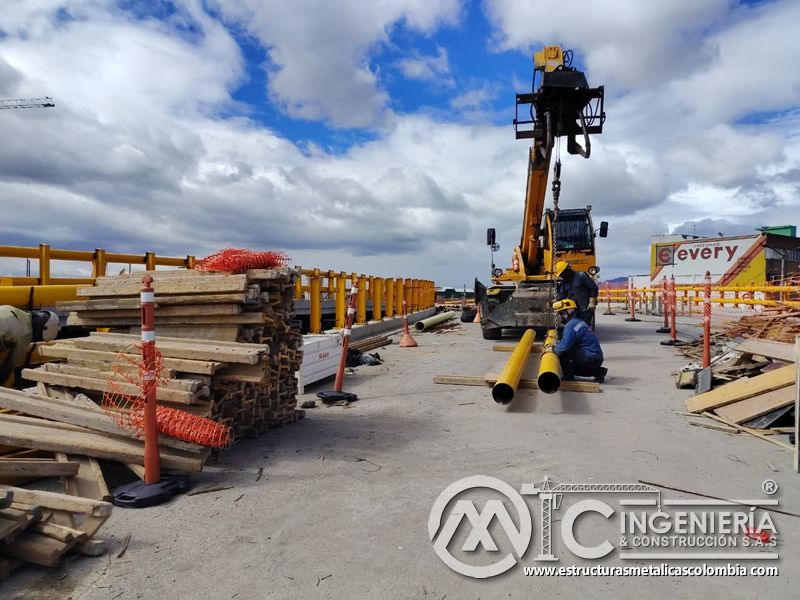 Prepare el izaje de tubos con cadenas, delimitación visible y una zona despejada frente a la maquinaria en Bogotá, Colombia. Montajes, Ingeniería y Construcción. MIC SAS.
