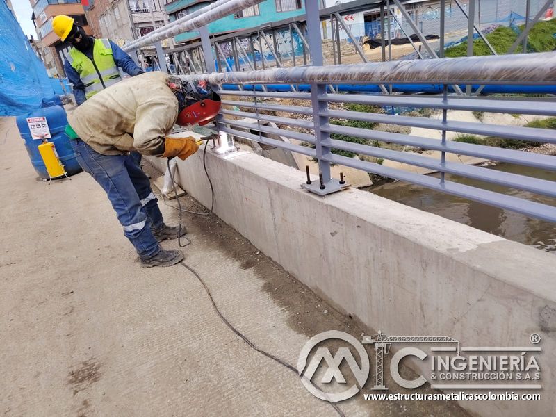 Fije travesaños grises al poste vertical mediante arco de soldadura y supervisión activa junto al canal en Bogotá, Colombia. Montajes, Ingeniería y Construcción. MIC SAS.