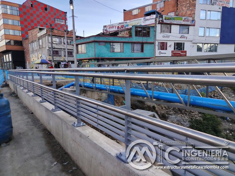 Descubra una baranda peatonal gris con pasamanos pulidos que protege el recorrido junto al canal urbano en Bogotá, Colombia. Montajes, Ingeniería y Construcción. MIC SAS.