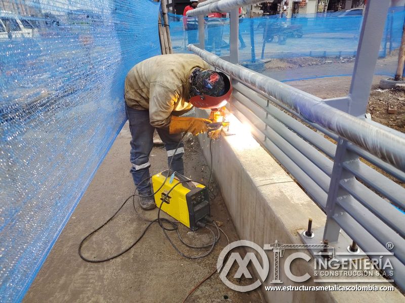 Finalice la unión inferior de la baranda gris mediante soldadura localizada sobre el murete de concreto en Bogotá, Colombia. Montajes, Ingeniería y Construcción. MIC SAS.