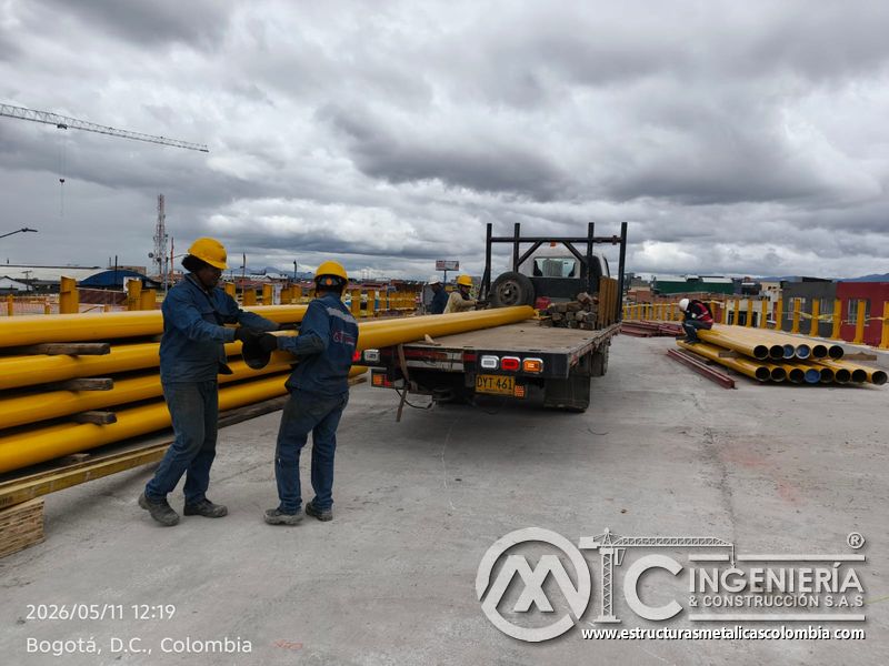 Observe cómo dos operarios movilizan un tubo metálico desde el camión hasta el depósito sobre el puente en Bogotá, Colombia. Montajes, Ingeniería y Construcción. MIC SAS.