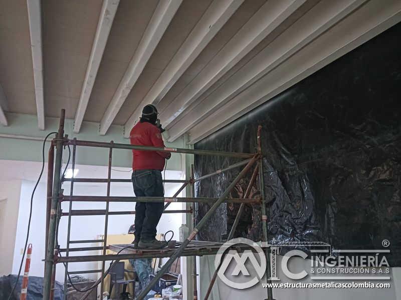 Operario aplica acabado blanco a viguetas del mezzanine metálico en Bogotá y Colombia. Montajes Ingeniería y Construcción. MIC SAS.