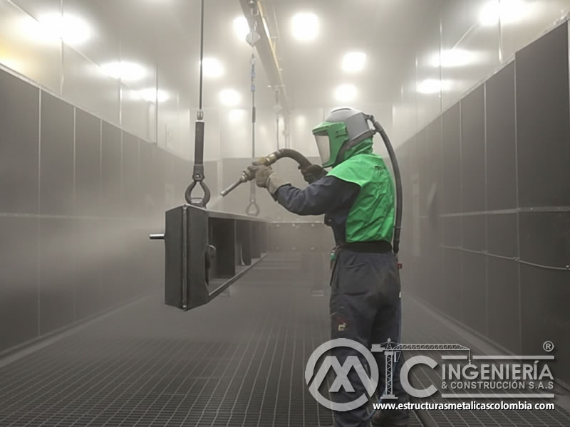 Operario con EPP chorreando abrasivo en cabina de sandblasting en Bogotá, Colombia. Montajes, Ingeniería y Construcción. MIC SAS.