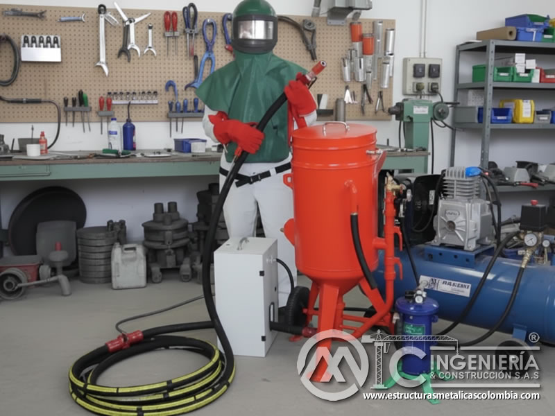 Operario con traje verde y EPP para el arenado con equipo portátil en Bogotá, Colombia. Montajes, Ingeniería y Construcción. MIC SAS.