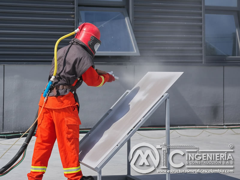 Operario con traje rojo aplicando sandblasting con granate en lámina metálica. Bogotá, Colombia. Montajes, Ingeniería y Construcción. MIC SAS.
